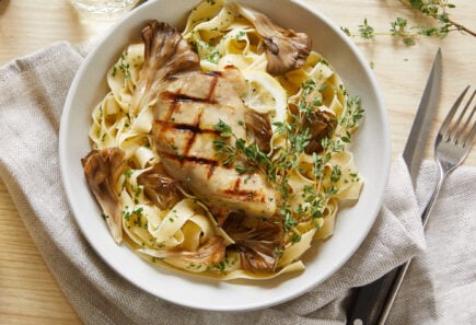 Cultivated grilled chicken on a bed of mushroom pasta and herbs viewed from above