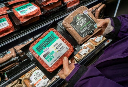 A shopper compares plant-based meat products in a supermarket aisle