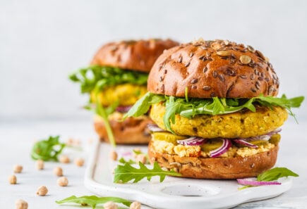 Plant-based burgers topped with arugula on a white stone counter