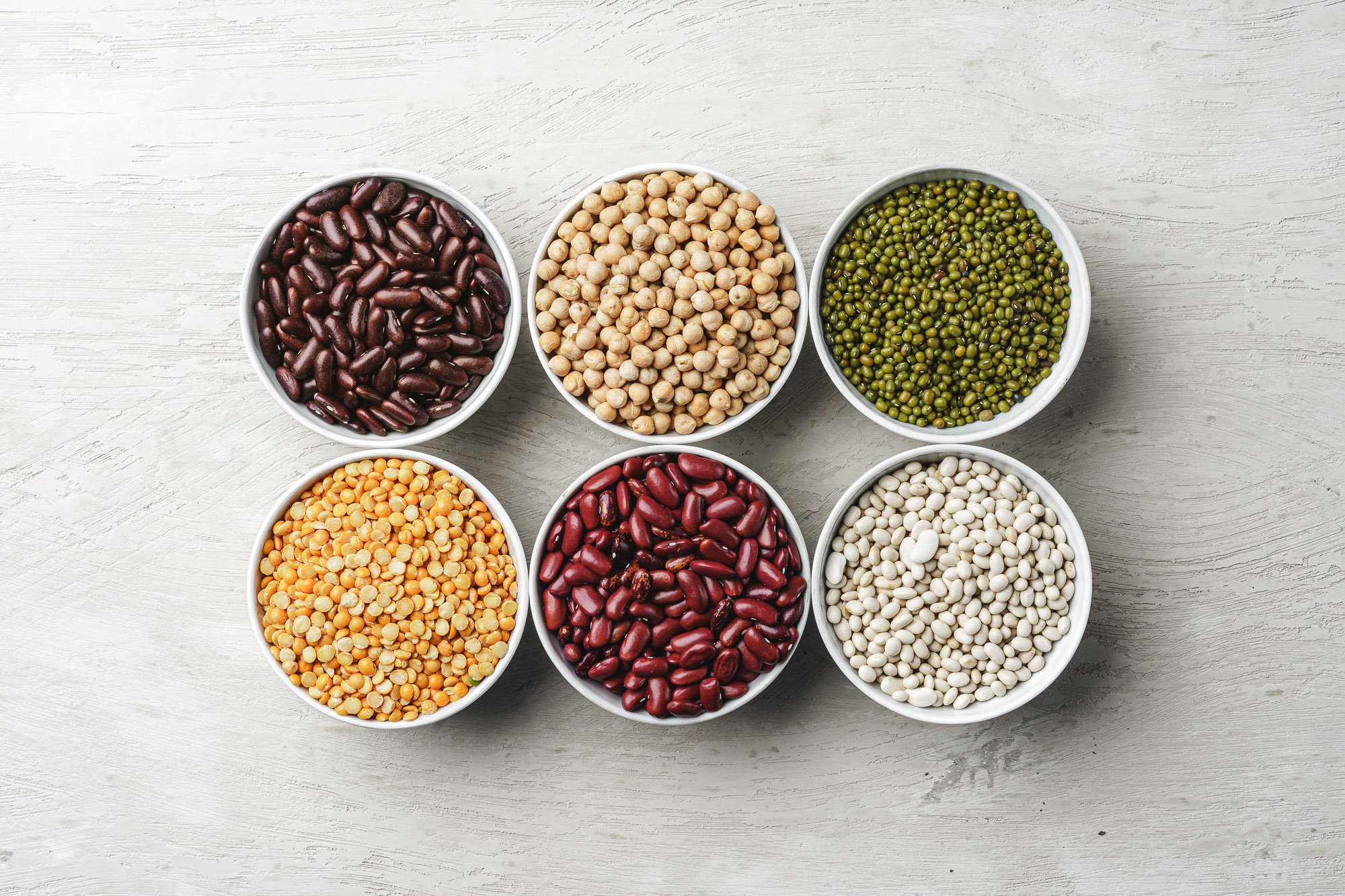 An assortment of beans in bowls on a white table, representing ingredients for plant-based meat