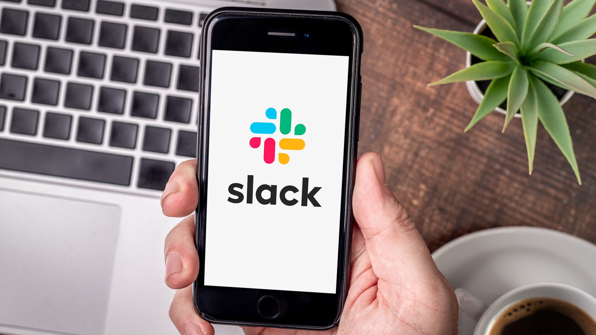 Slack mobile app on a smartphone screen, held by a person over their desk