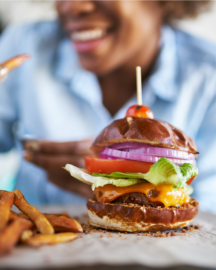 A smiling woman enjoying a delicious plant-based burger and thick-cut fries